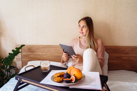 In the morning beautiful caucasian lady sitting and drinking hot tea or coffee in bed. Blond female solving work issues remotely. Cozy workplace at home. Distance learning online education and work.の写真素材