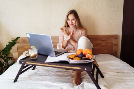 Attractive, blonde Caucasian ethnicity emotionally communicates via video, using tablet or computer. Adds gestures to speech. Looking at screen in front of her and showing stop sign, arms crossed.の写真素材