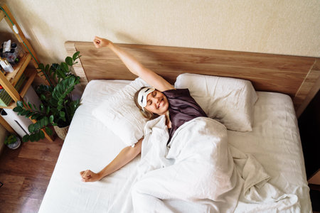 A beautiful blonde stretching sweetly in her bed on an early sunny summer morning. Lazy weekend. The freelancer himself creates the schedule of his day. Top view. Lying in the bed. Hands to the side.の写真素材