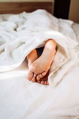 Early morning sleep concept. A funny shot of naked legs, feet of a girl sticking out from under the...