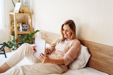 Young, pretty, attractive, charming girl blonde of European appearance, is smiling widely on tablet with friends and relatives. Using video communication, friendly waving hand, looking at the screen.の写真素材