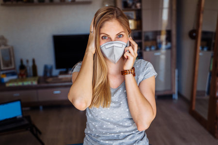 Attractive girl, wearing face mask, calling on the phone and holding her head in horror due to the large number of ill patients with  epidemy.  pandemy.の写真素材