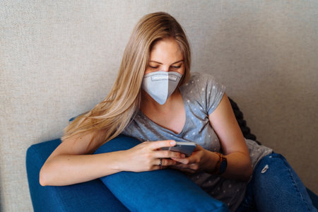 Casual girl in a protective face mask is phoning on labor issues. Isolated at home due to  and high risk of getting sick and die.の写真素材