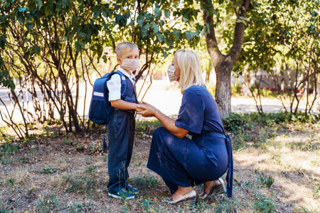 Mom is ready to send her little son to first grade. Gently holds the boy's hands. They are wearing protective medical masks. New requirements for training during the quarantine periodの写真素材