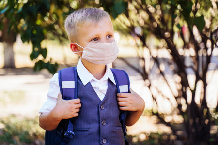 new rules for staying at school. An elementary school student goes to school in the morning. Always wear a protective medical mask. Looks smart and neat in a new uniform.の写真素材