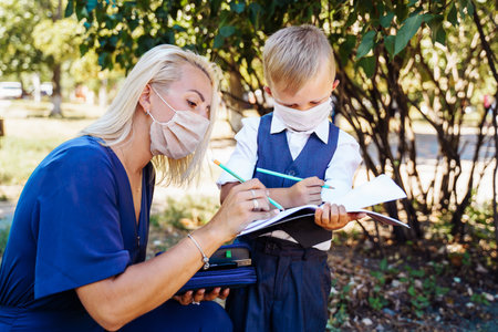 Mom tells her son what awaits him at school. They hold a notebook in their hands and make notes. They use protective medicalの写真素材