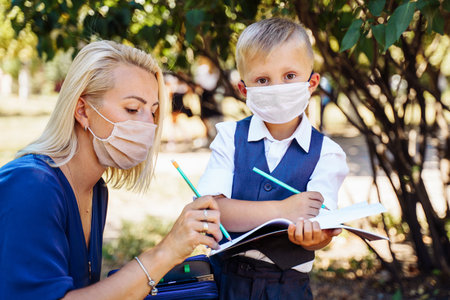 Mom tells her son what awaits him at school. They hold a notebook in their hands and make notes. They use protective medical masksの写真素材
