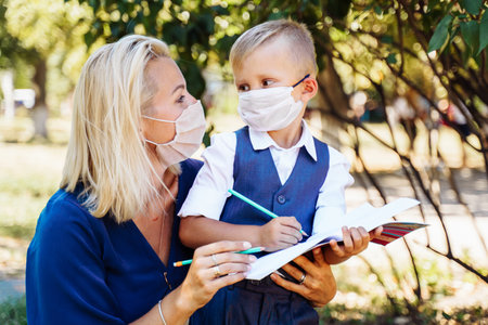 Mom tells her son what awaits him at school. They hold a notebook in their hands and make notes. They use protective medical masks  epidemic.の写真素材