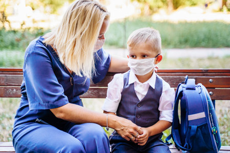 Mom and her son, a schoolboy, are sitting on a bench in the yard. They put on medical masks to protect themselves from the  . Important methods of protectionの写真素材
