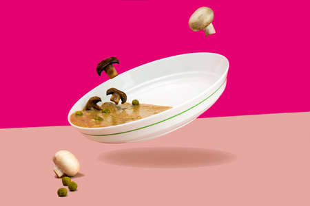 Levitating food Flying mushrooms. Mushroom cream soup champignons in a white plate On a bright pink background of fuchsia green peas. copy spaceの写真素材