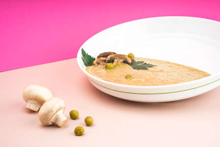 Levitating food Flying mushrooms. Mushroom cream soup champignons in a white plate On a bright pink background of fuchsia green peas. copy spaceの写真素材