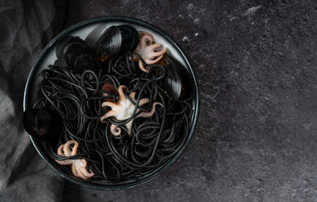 Concept Mediterranean delicacy food. Black seafood spaghetti pasta with octopus and mussels with gray napkin in a black plate on a dark background. Copy Spaceの写真素材