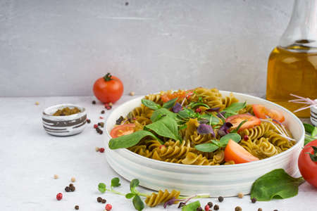 Green spinach pasta with microgreen and tomato and pesto and pepper in a white bowl with silver cutlery. Gourmet italian meal. Side view. Copy spase. Mock up. concept health eatingの写真素材