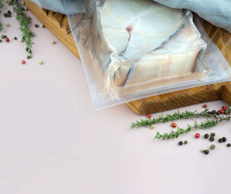 Sous-vide cooked technology concept. Vacuum fillet of fresh atlantic white fish on wooden board with...