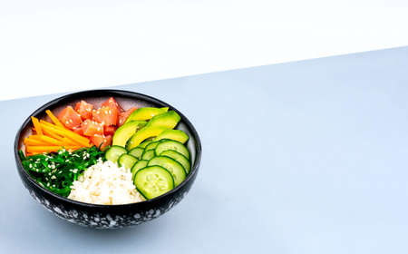 An overhead diagonal, isometric projection photo of poke bowl, traditional Hawaiian and Japanise raw fish salad, from seaweed, rice, salmon, cucumber, soy sause and avocado. with chopsticks and sesame seeds. Copy space, on a blue and white backgroundの写真素材