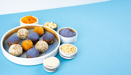 Homemade blue matcha energy balls in a ceramic bowl plate on a bright blue background top view, healthy sweets made of nuts and date, dried apricots, sesame, cashew nuts. Concept vegeterian diet sweet brain food. Copy spaceの写真素材