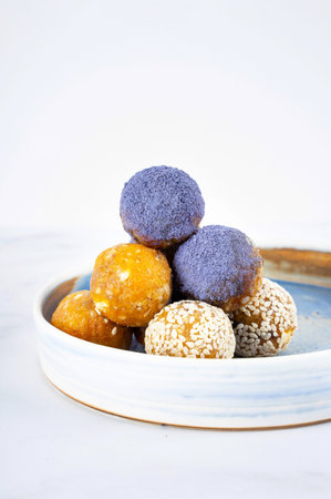Homemade blue matcha energy balls in a ceramic bowl plate on a bright marble background top view, healthy sweets made of nuts and date, dried apricots, sesame, cashew nuts. Concept vegeterian diet sweet brain food. Copy spaceの写真素材