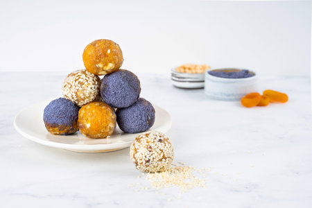 Homemade blue matcha energy balls in a ceramic bowl plate on a bright marble background top view, healthy sweets made of nuts and date, dried apricots, sesame, cashew nuts. Concept vegeterian diet sweet brain food. Copy spaceの写真素材