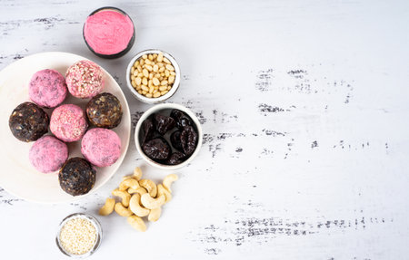 Homemade pink matcha energy balls in a ceramic plate on a white wood background top view, healthy sweets made of nuts and date, dried apricots, prunes, sesame, cashew nuts, Pine nuts. Concept vegeterian diet sweet brain food. Copy spaceの写真素材