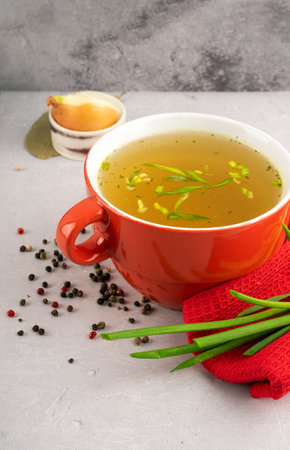 hot homemade vegeterian vegetable broth with amino acids in red bowl with red napkin and green onions, black peas, chopped white onions and carrots on gray background. Concept support the immune systen and functional ingredientsの写真素材