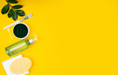 Green Spirulina DIY facial cleansing mask and ingredients. Concept Stay home treat yourself. Spa, beauty cosmetics and body care. Top view flat lay: bath accessories, bowl, podium on yellow backgroundの写真素材