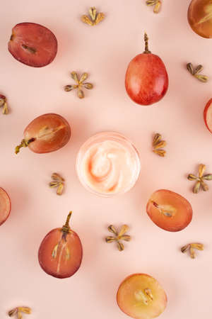 Concept organic extract nature grape seeds oil in cream for skin care in home. Creative modern flat lay composition with fresh red grapes and seeds in pink background. Naturecore. Eco. Close up.の写真素材