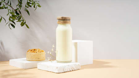 Vegetable pea milk in a bottle and peas in handmade ceramic bowl on white podium, pedestal on beige background. shadows from green foliage.Gluten-free, lactose-free vegan product. Modern. Copy spaceの写真素材