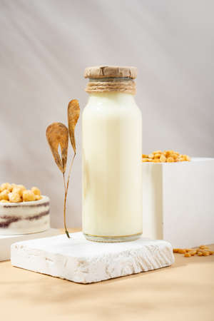Vegetable pea milk in a bottle and chick peas in handmade ceramic bowl on white podium, pedestal on beige background. shadows. dry leaves. Gluten-free, lactose-free vegan product. Modern. Copy spaceの写真素材