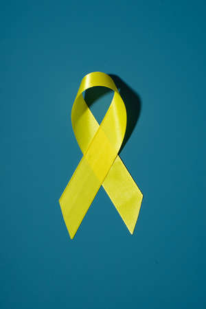Yellow cancer awareness ribbon as symbol of childhood cancer awareness on blue background. Copy spaceの写真素材