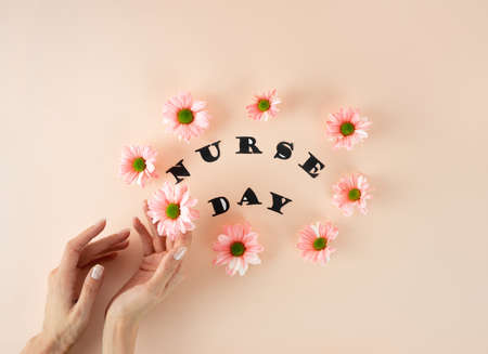 Female hands hold a pink chrysanthemum on a pastel pink background with a white medical mask. Lettering. Floral postcard concept. Top view with copy space. National Doctor's Day. Happy nurse dayの写真素材