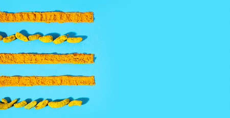 Dried turmeric roots with turmeric powder laid out in a line on a light blue background.Trending...
