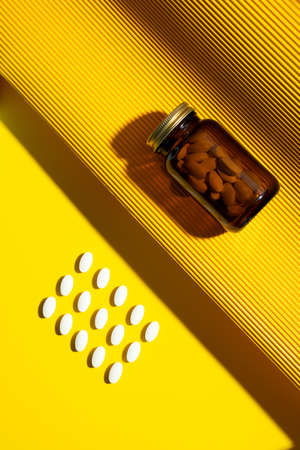 Vitamin capsules. Vitamin C pills and pill glass bottle on yellow background with trendy shadows. Concept wellness and heathy lifestyle. Modern minimalistic photo. Monochromatic.Top view. Copy space.の写真素材