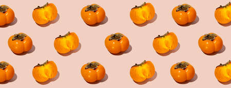 Colorful fruit pattern of fresh whole and sliced organic persimmon fruit with leaves on beige-pink...