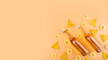 A two bottles of craft lager and porter beer and nachos snack and pistachios on beige background. International beer day or Octoberfest concepts. Minimalistic photo. Copy spaceの写真素材