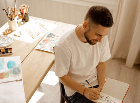 Portrait of Young dark haired concentrated caucasian white male artist with a beard in a white...