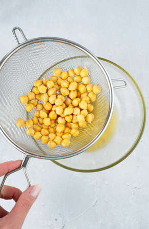 Chickpea water aquafaba. Egg replacement. Vegan concept. Metal sieve draining aquafaba chickpea water into glass bowl. on a gray background. sustainable lifestyle and natural eco-friendly products.の写真素材