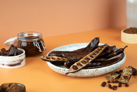 Organic carob pods, seeds in a ceramic plate on a beige background, locust bean healthy food, Ceratonia siliqua harnup. Natural vegan eating. creative food background. Copy space. Diagonal projectionの写真素材