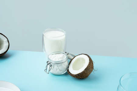 Coconut products. Cracked open coconut with meat cut in half, coconut powder in a glass jar, plant milk on a blue background. isometric projection. Copy space. Concept alternative milk, vegeterianの写真素材