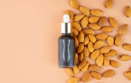 Creative layout. Natural almond oil in a matte glass bottle and scattering of almonds on a pastel beige background. The concept of skin care, beauty and health. Top view, copy spaceの写真素材