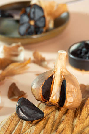 Fermented garlic head and garlic clove on a handmade wooden plate. A small clay bowl with black garlic paste in the background. Healthy and fermented food photo composition, selective focus.の写真素材