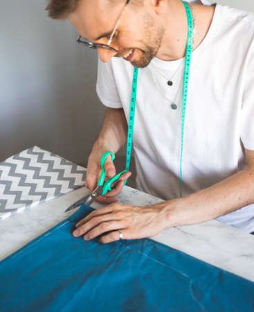 Sewing clothes for pets. Tailoring clothes for cats. A laughing tailor in white t-shirt is sewing...
