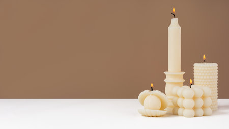 Handmade olive wax different forms burning candle on a duotone brown and white background. Sustainability vegan candle, natural materials. Minimalistic, cozy atmosphere modern photo.Copy space.Bannerの写真素材