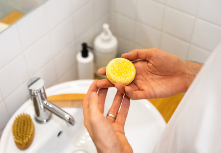 Man in the bathroom holding a solid shampoo bar. Plastic free, zero waste living, low water ingredients. sustainable hair care. Choosing responsibility for the nature, life style composition.の写真素材