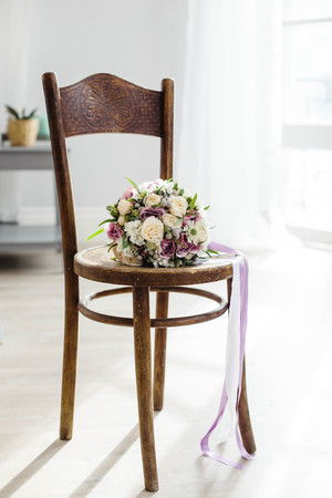 Bridal bouquet. The bride's . Beautiful of white flowers and greenery, decorated with silk ribbon, lies on vintage wooden chairの写真素材