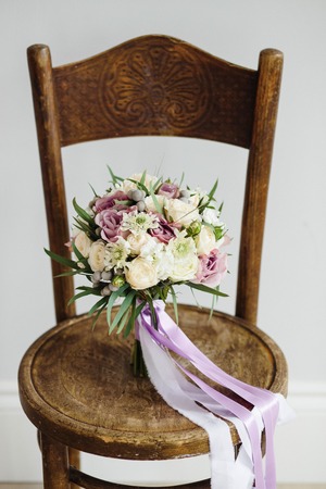 Bridal bouquet. The bride's . Beautiful of white flowers and greenery, decorated with silk ribbon, lies on vintage wooden chairの写真素材