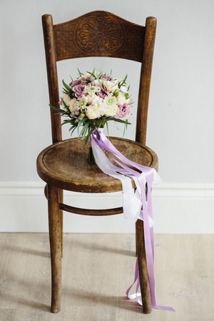 Bridal bouquet. The bride's . Beautiful of white flowers and greenery, decorated with silk ribbon, lies on vintage wooden chairの写真素材