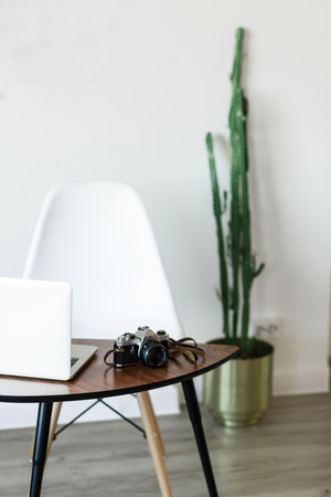 Minimal working place at home with computer, photocamera and cactus near white wallの写真素材