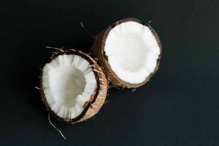 Broken ripe coconut on black background. brown peel and white fleshの写真素材