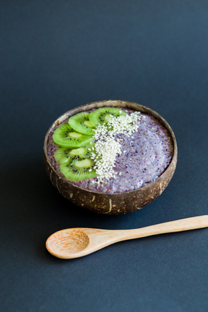 Healthy smoothie with fruits, plate made from coconut shell and wood spoon. Kiwi, banana, black currantの写真素材