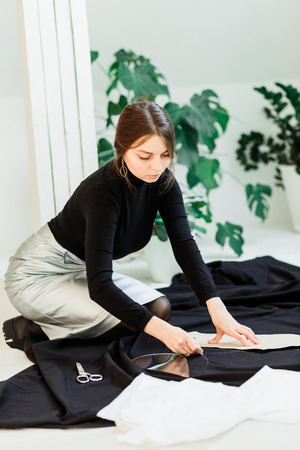 Beautiful seamstress, cut black fabric on the studio floor,draws on fabricの写真素材